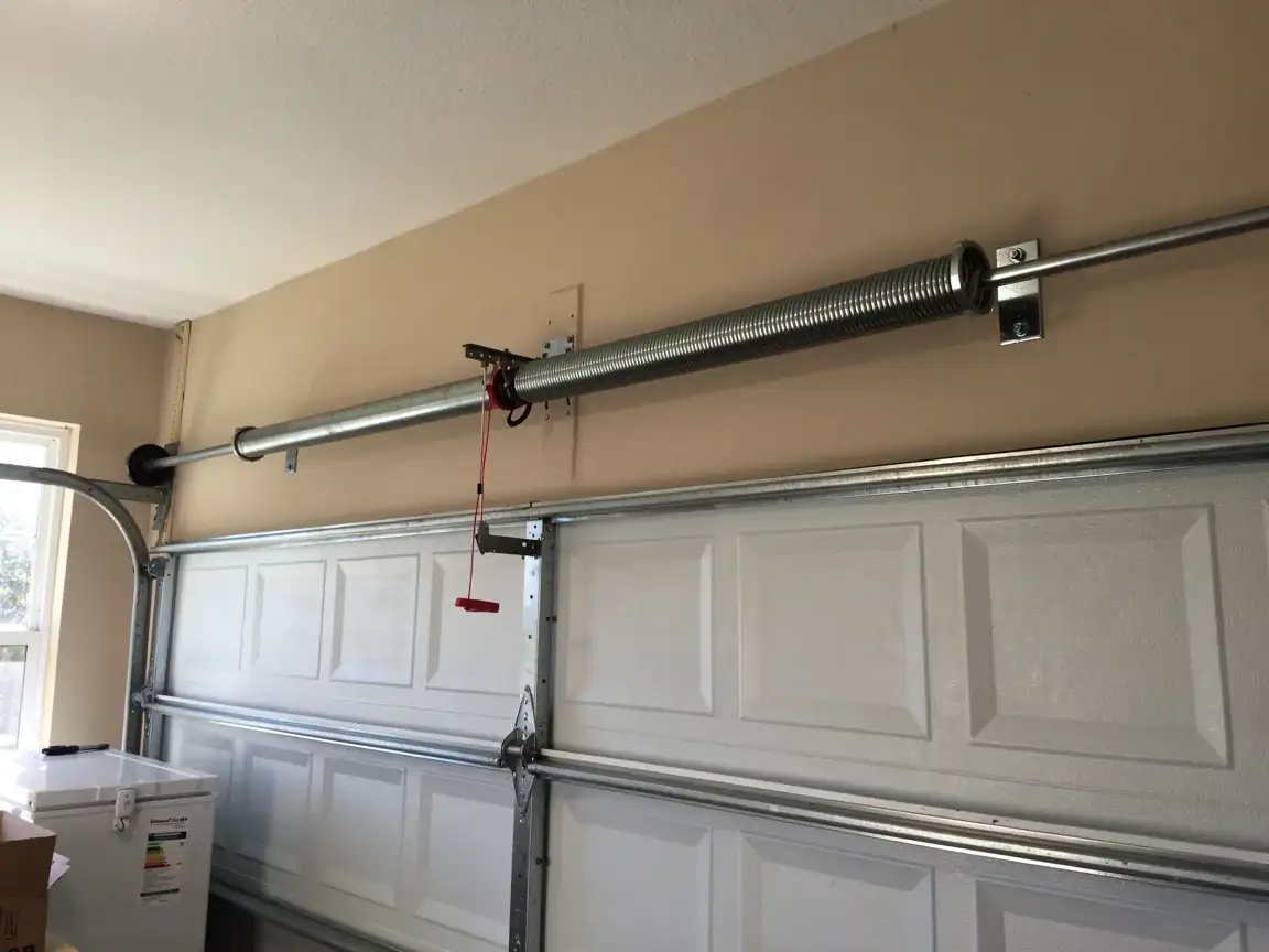 A torsion spring is mounted above a white garage door.